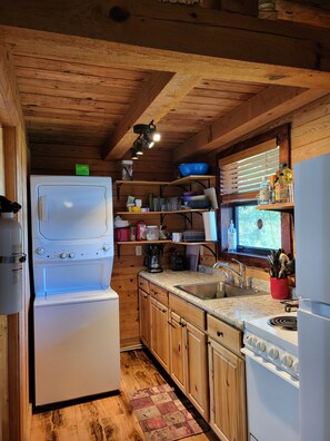 A compact kitchen with wooden cabinets, a built-in oven, a sink, and a window with blinds.