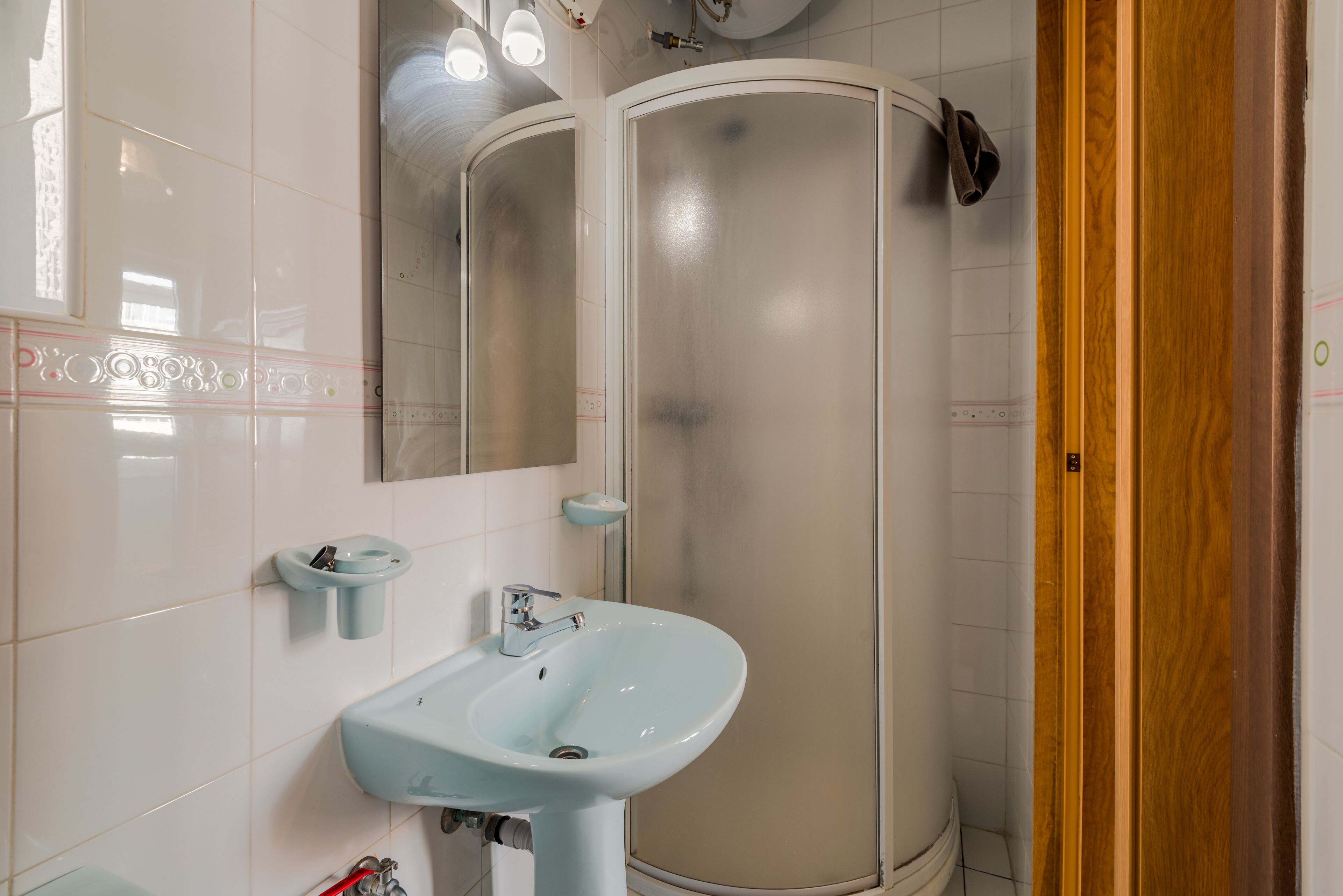 Un baño con lavamanos blanco, espejo y cabina de ducha.