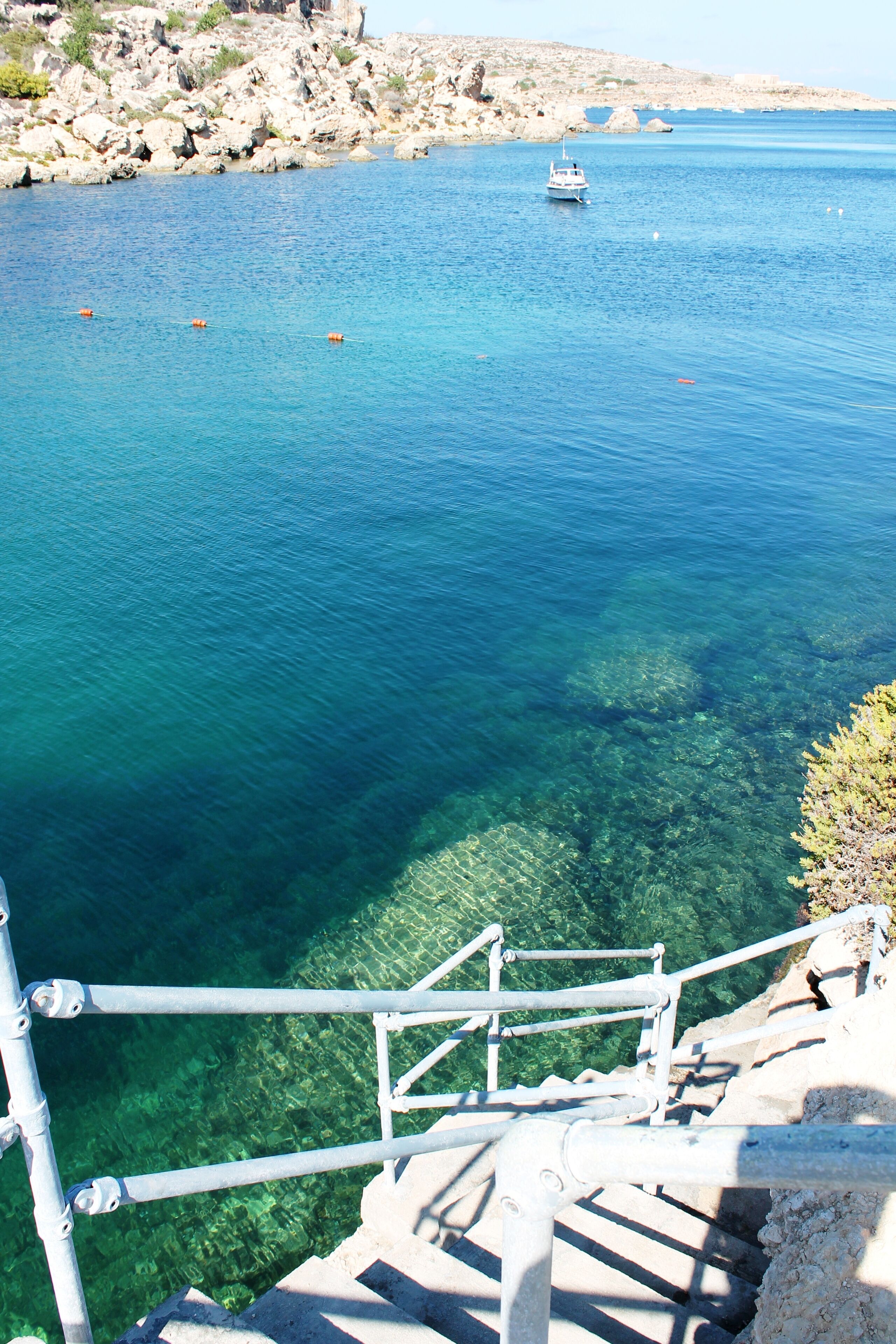 Une vue dégagée sur une zone côtière, avec un bateau sur l’eau, un terrain rocheux et un escalier menant à la plage.