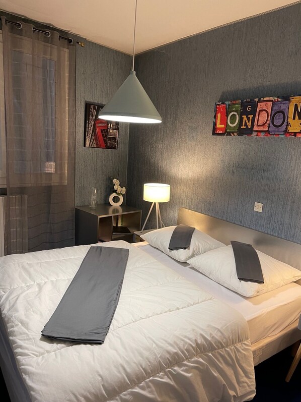 A hotel room with a bed, a desk, a lamp, and a wall with a London-themed decoration.