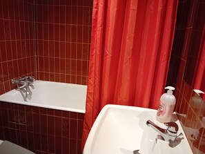 A bathroom with a white bathtub, a white sink, and a red shower curtain.