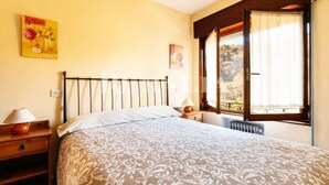 Een slaapkamer met een bed, nachtkastje, lamp, poster aan de muur en een raam met gordijnen.