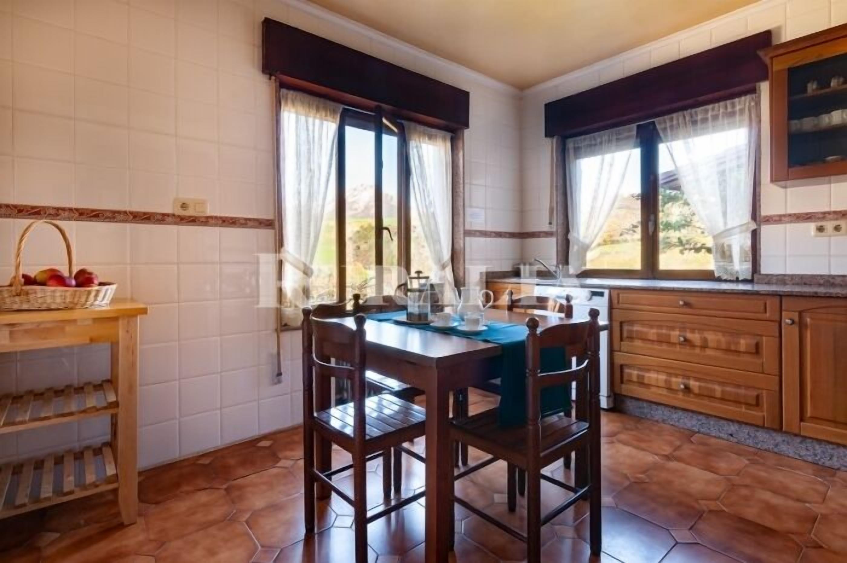 A kitchen with a dining table, chairs, a fruit basket, and a window with curtains.