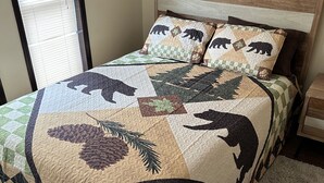 A bed with a quilt featuring bear and pinecone patterns, a wooden headboard, and a small bedside table.