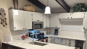 A modern kitchen with white cabinets, a large island with stools, a built-in oven, and a hanging light fixture.