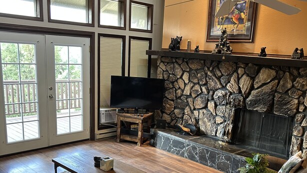 A spacious living room with a stone fireplace, a ceiling fan, and a large TV.