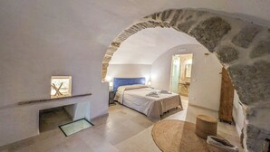 A room with a stone archway, a bed with a blue headboard, a bedside table, and a woven rug. - Case al Borgo - Albergo diffuso (Agira)