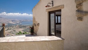 A balcony with a view of a coastal landscape, a potted plant, and a door leading to a room. - Case al Borgo - Albergo diffuso (Agira)