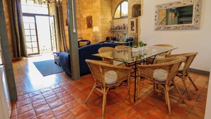 Un comedor con sillas de mimbre y una mesa de cristal, una pared de piedra y vistas a través de una puerta abierta.