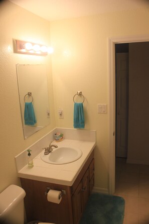 Un baño con lavabo, espejo e inodoro. Hay dos toallas colgadas en ganchos.