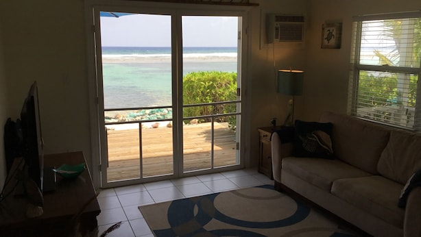 Una habitación con un amplio ventanal corredera que da a una terraza de madera con vista a la playa.