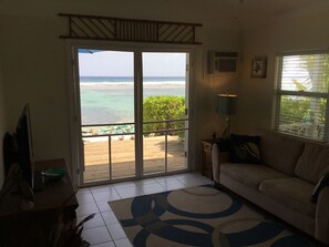 Una habitación con un amplio ventanal corredera que da a una terraza de madera con vista a la playa.