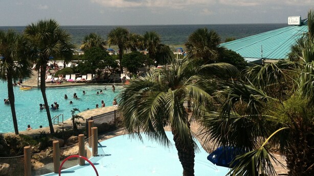 A pool area with clear blue water, surrounded by palm trees and a view of the ocean. -  Beautiful Ocean Front, Deluxe 2 BR/BA , Free Wifi, Prime Location. (Panama City Beach)