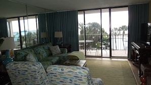 A hotel room with a large balcony, a sofa, a dining table, and a TV. -  Beautiful Ocean Front, Deluxe 2 BR/BA , Free Wifi, Prime Location. (Panama City Beach)