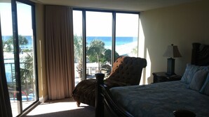 A bedroom with a large window offering a view of the beach and palm trees. -  Beautiful Ocean Front, Deluxe 2 BR/BA , Free Wifi, Prime Location. (Panama City Beach)