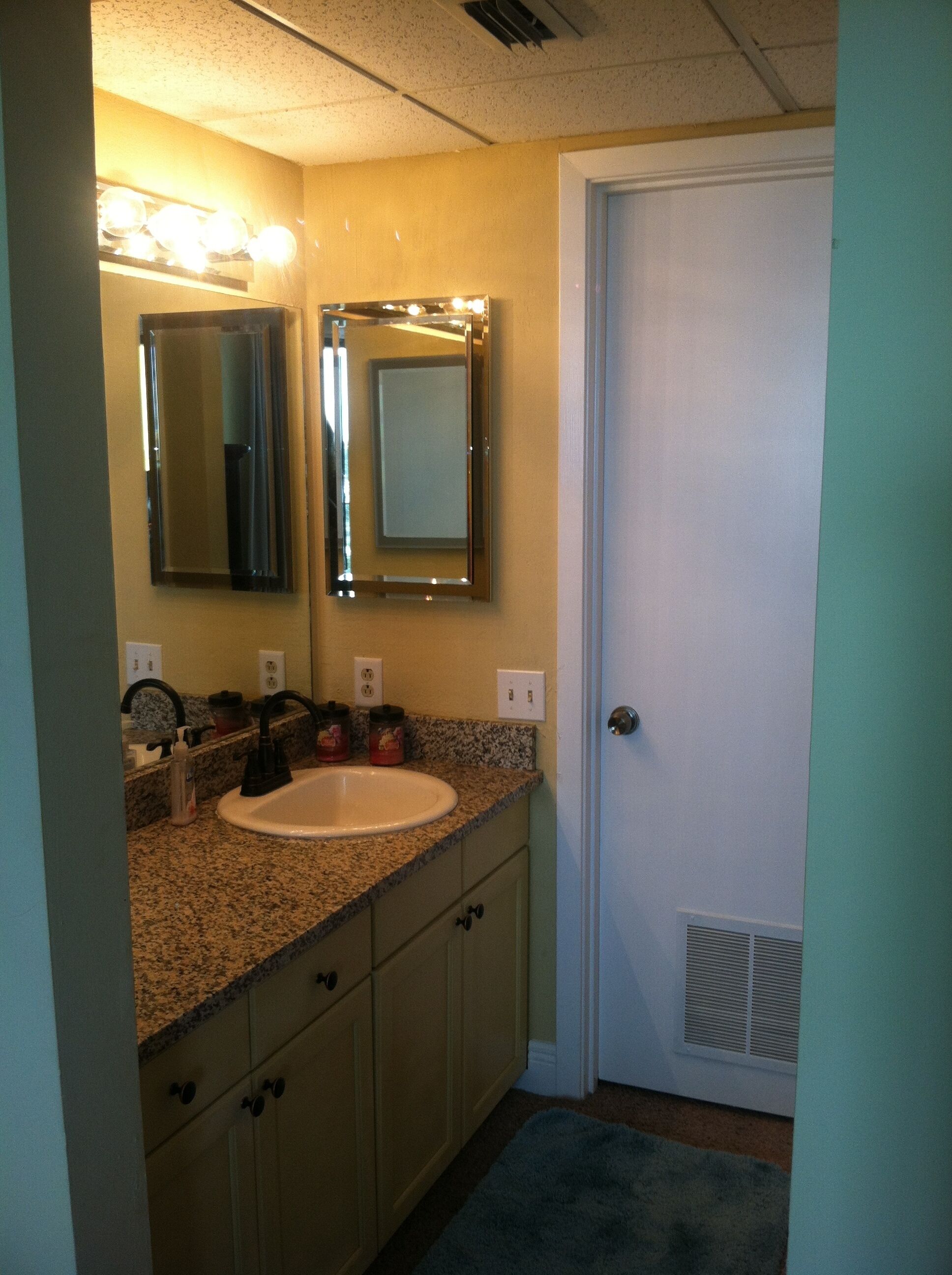 Une salle de bain avec un lavabo, deux miroirs, un meuble-lavabo et une porte.