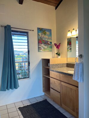 A bathroom with a window, a painting, a sink, and a mirror. - OCEAN VIEW, WALK TO BEACH, SLEEPS 8, POOL & HOT TUB, 3BDR + PRIVATE MASTER SUITE (Kihei)