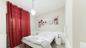 Ein Schlafzimmer mit einem Bett, einem Nachttisch, einem roten Vorhang und Wandkunst.