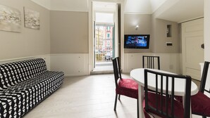 Ein modernes Wohnzimmer mit einem schwarz-weißen Sofas, einem Esstisch mit Stühlen, einem Fernseher und Blick auf die Stadt durch eine Tür.