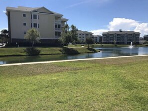 A residential area with modern apartment buildings, a grassy lawn, and a small pond with a fountain. - Stunning 1st Floor, 3 Bedroom in Myrtlewood Villas (Myrtle Beach)