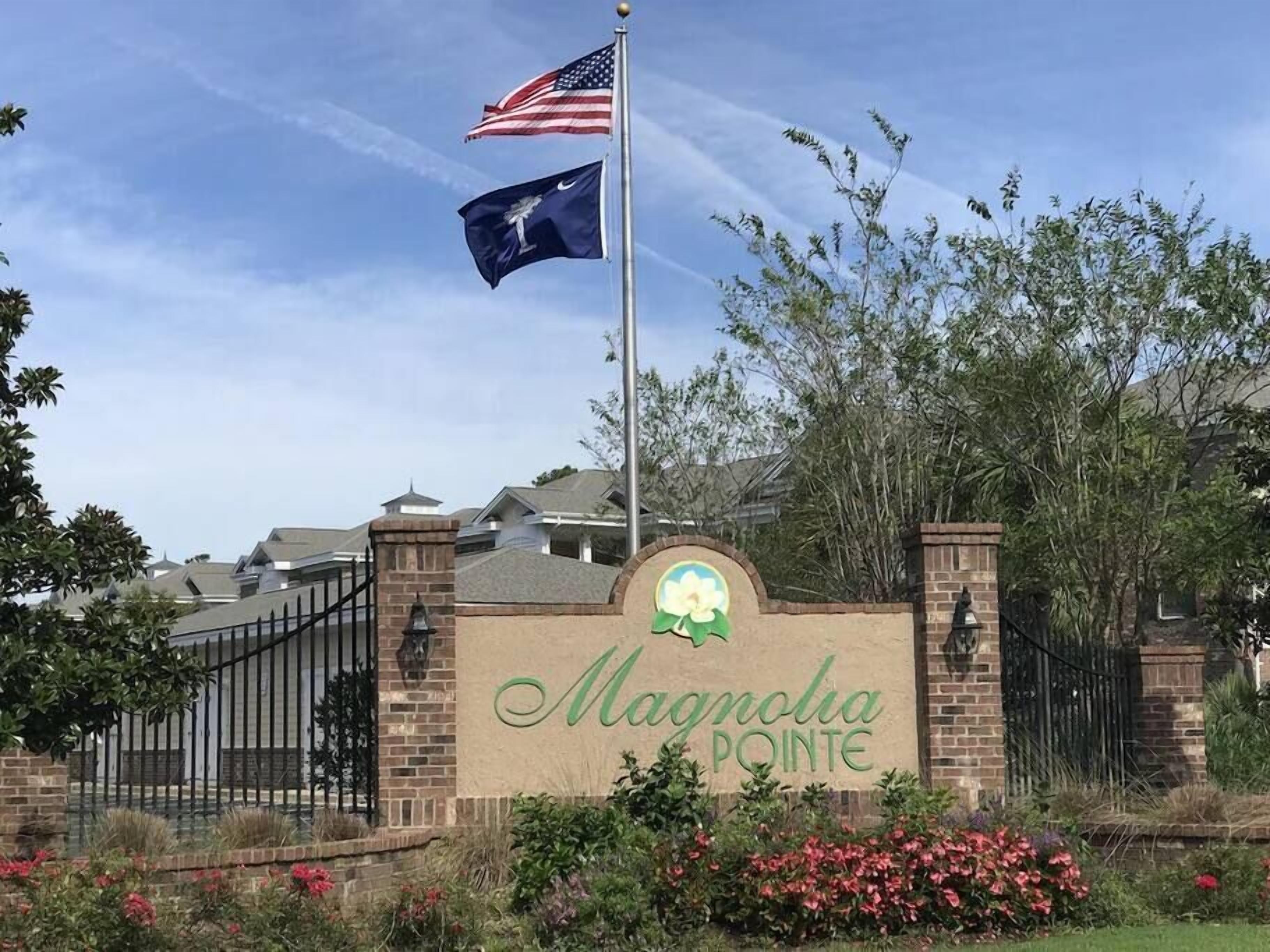 A gated entrance with a sign reading "Magnolia Pointe" and two flags, one of the United States and one with a logo.