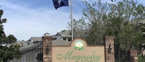 A gated entrance with a sign reading "Magnolia Pointe" and two flags, one of the United States and one with a logo.