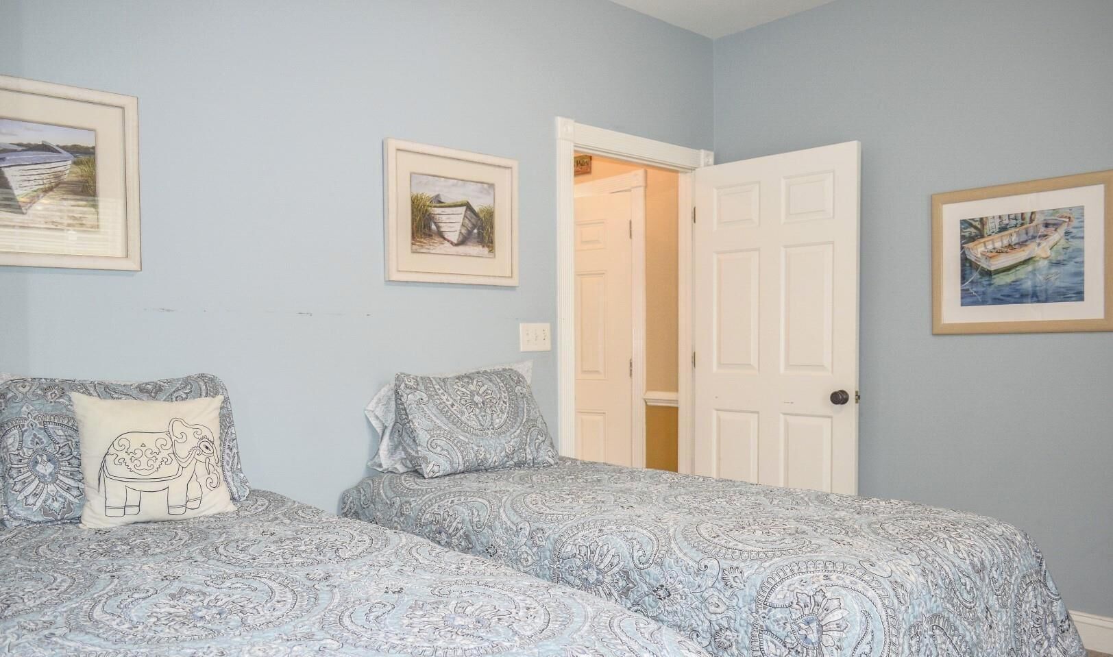 A bedroom with two beds, each with patterned bedding, a door leading to another room, and framed artwork on the walls.
