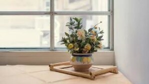 Um quarto com uma janela grande, uma mesa com um vaso de flores e uma cadeira de vime.