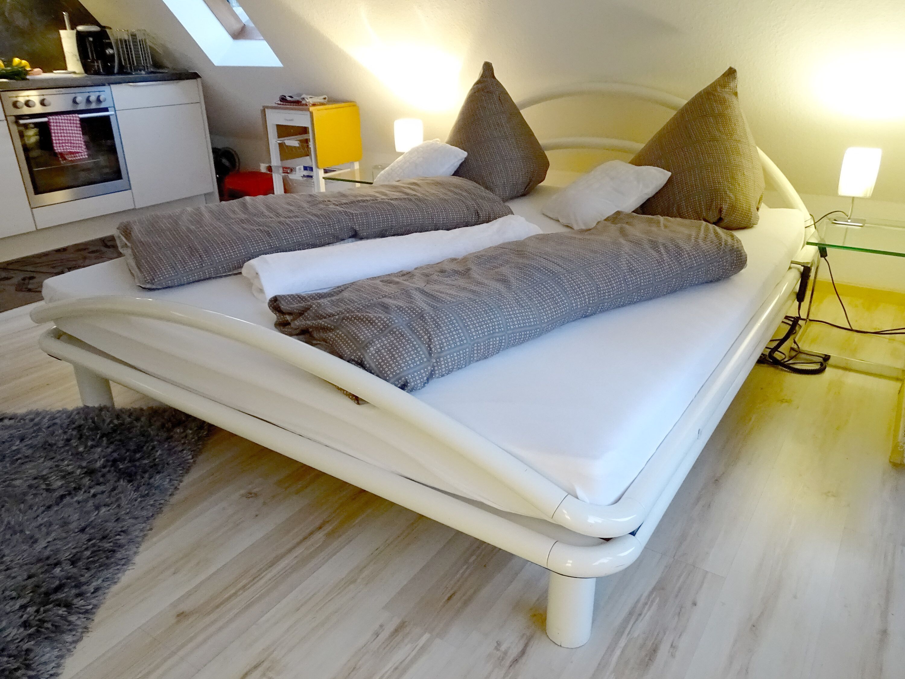 A modern bedroom with a bed, pillows, and a bedside table with a lamp.
