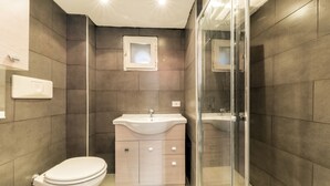 A modern bathroom with a toilet, sink, and glass shower enclosure. - Chia Deluxe (Naples)
