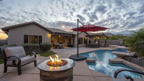 Patio trasero con piscina, mobiliario exterior y una chimenea.
