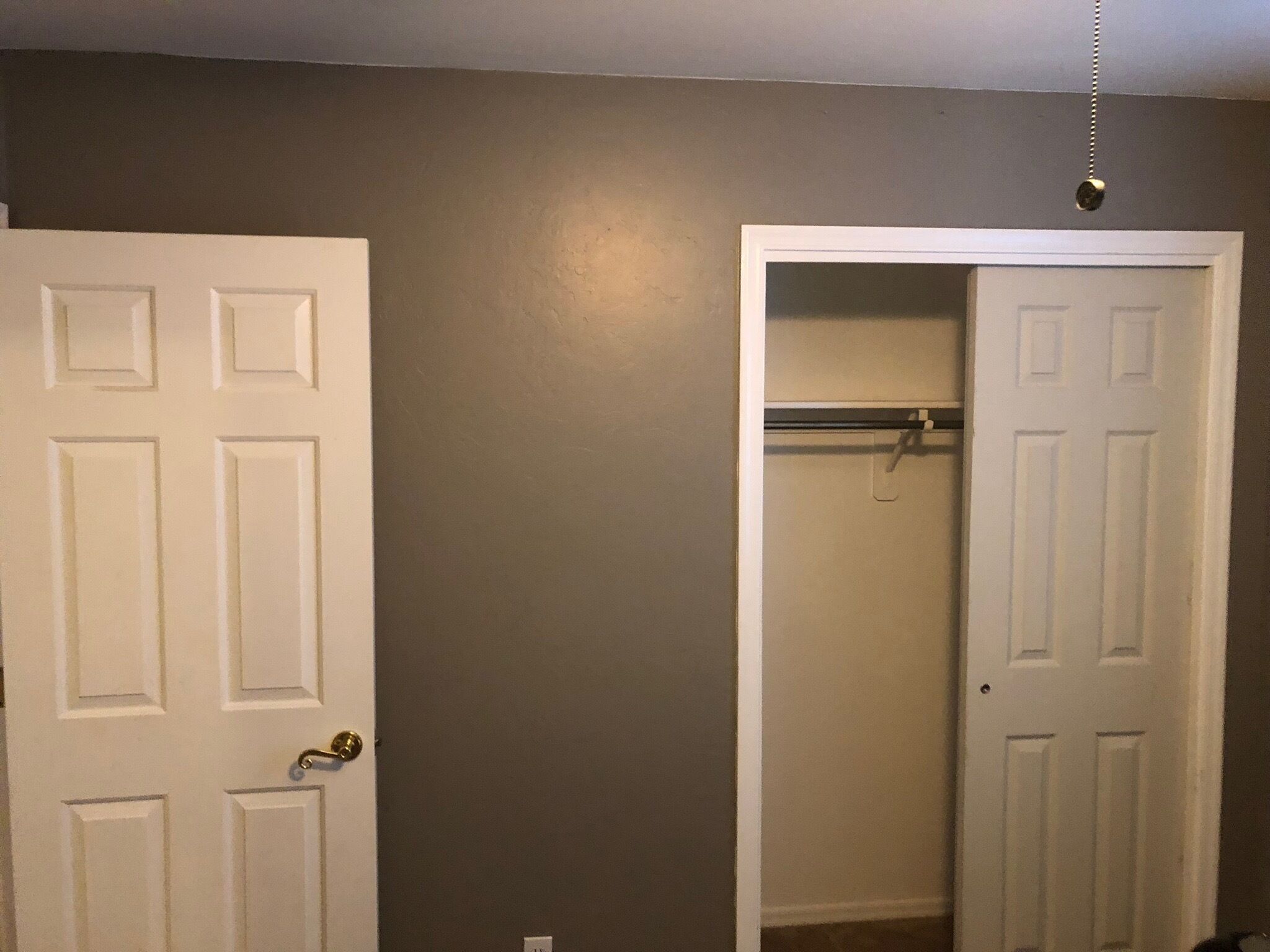A room with a white door, a closet with a hanging rod, and a light switch on the wall.