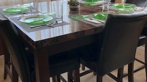 Una mesa de comedor dispuesta con platos verdes, vasos y cubiertos, rodeada de sillas.