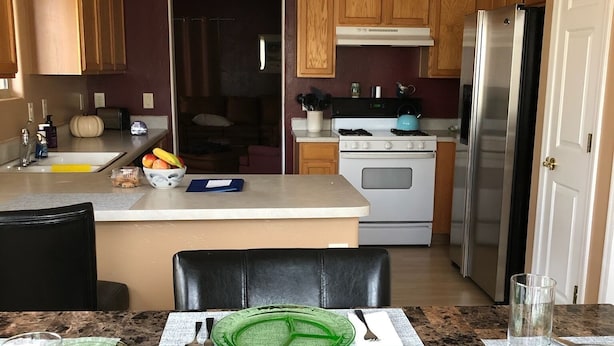 Una cocina con armarios de madera, un refrigerador de acero inoxidable, una estufa y un comedor con una mesa de mármol para dos personas.