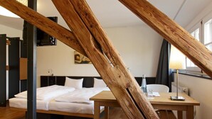 A room with a sloped ceiling, wooden beams, a bed, a desk, and a chair. - OX Hotel Café Bar Restaurant (Heitersheim)
