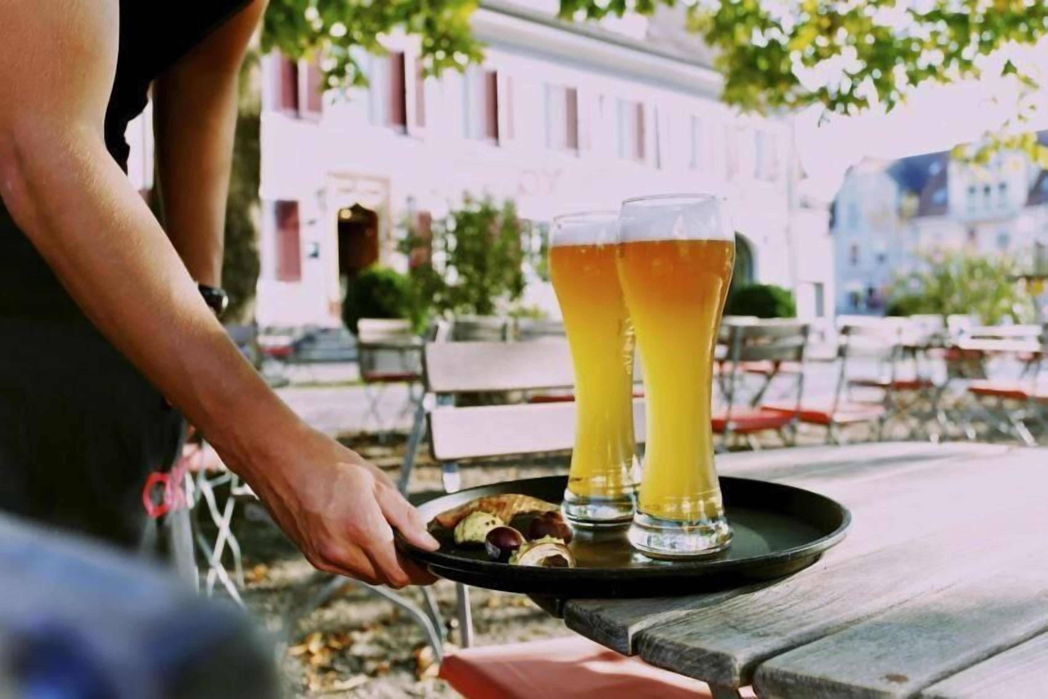 A person carrying a tray with two glasses of beer and a plate with food items.