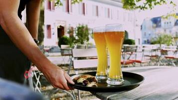 A person carrying a tray with two glasses of beer and a plate with food items.
