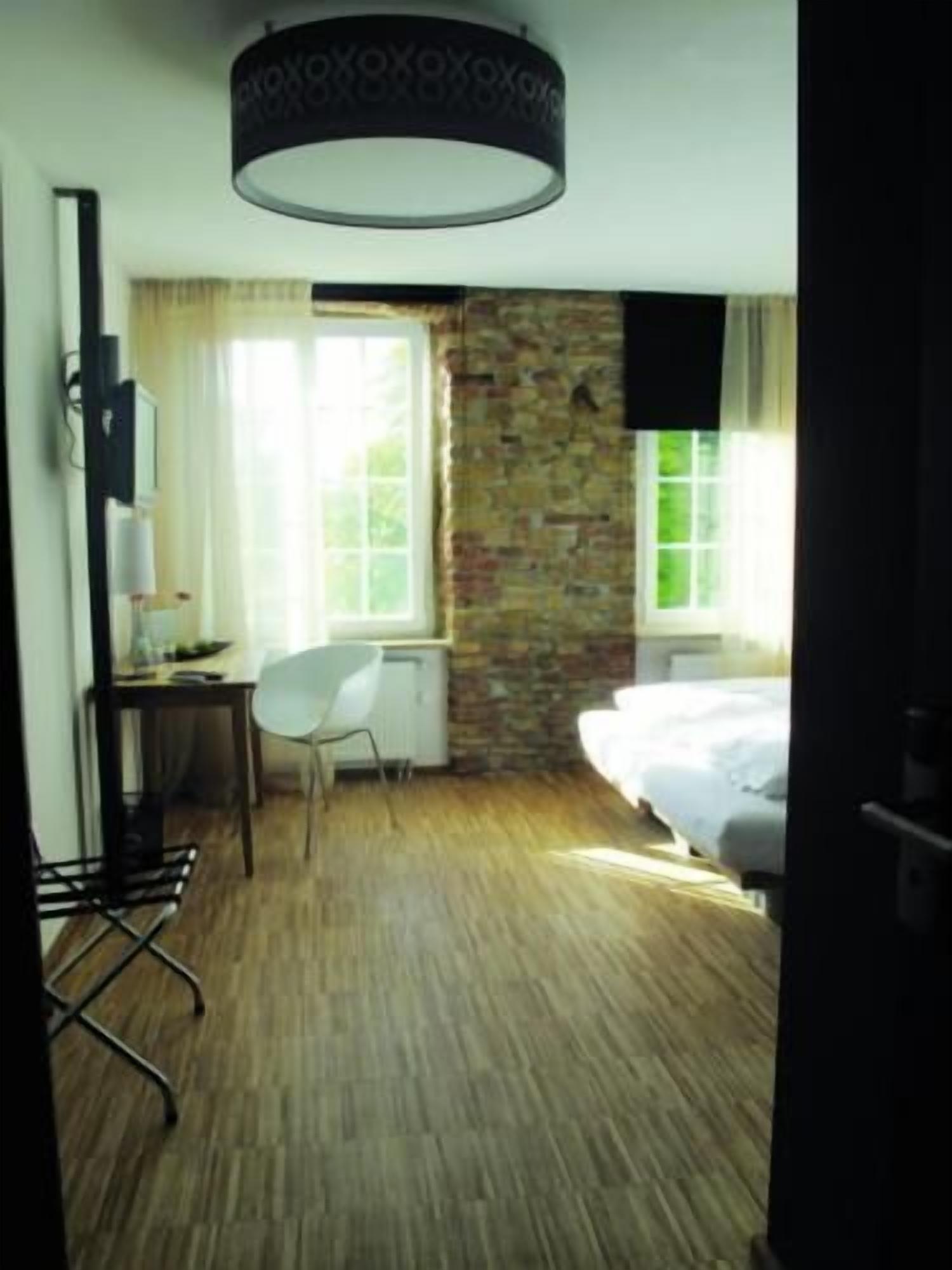 A hotel room with a bed, a desk with a chair, a TV, and a window with curtains.