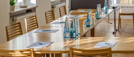 Un salón de conferencias con una larga mesa, sillas de madera y botellas de agua sobre la mesa.