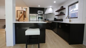 Una cocina moderna con armarios negros, encimera blanca, electrodomésticos de acero inoxidable y una escalera de madera.
