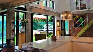 Une cuisine moderne dotée d’un grand îlot central, d’un coin repas avec des sièges extérieurs et d’une vue sur un jardin.