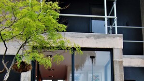 L’entrée d’un immeuble avec une porte en verre, un banc à l’extérieur et un arbre aux feuilles vertes.