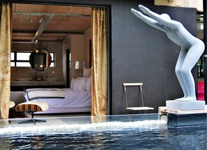 A modern hotel room with a bed, a desk, and a sculpture by the pool. - The Bright House Villa (Oudtshoorn)