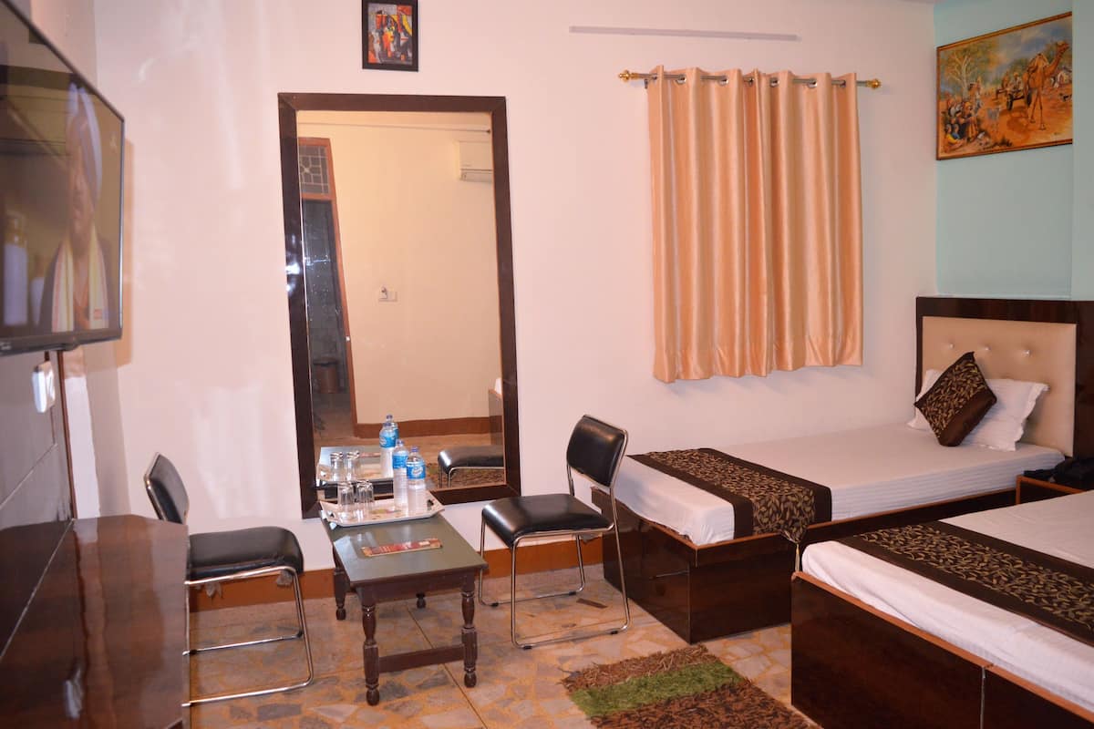 A hotel room with two single beds, a desk with a chair, a television, and a bathroom visible through a door.