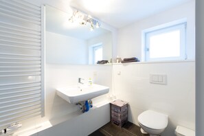 A modern bathroom with a white sink, a mirror, a toilet, and a window. - Hannover Business Apartments (Hannover)