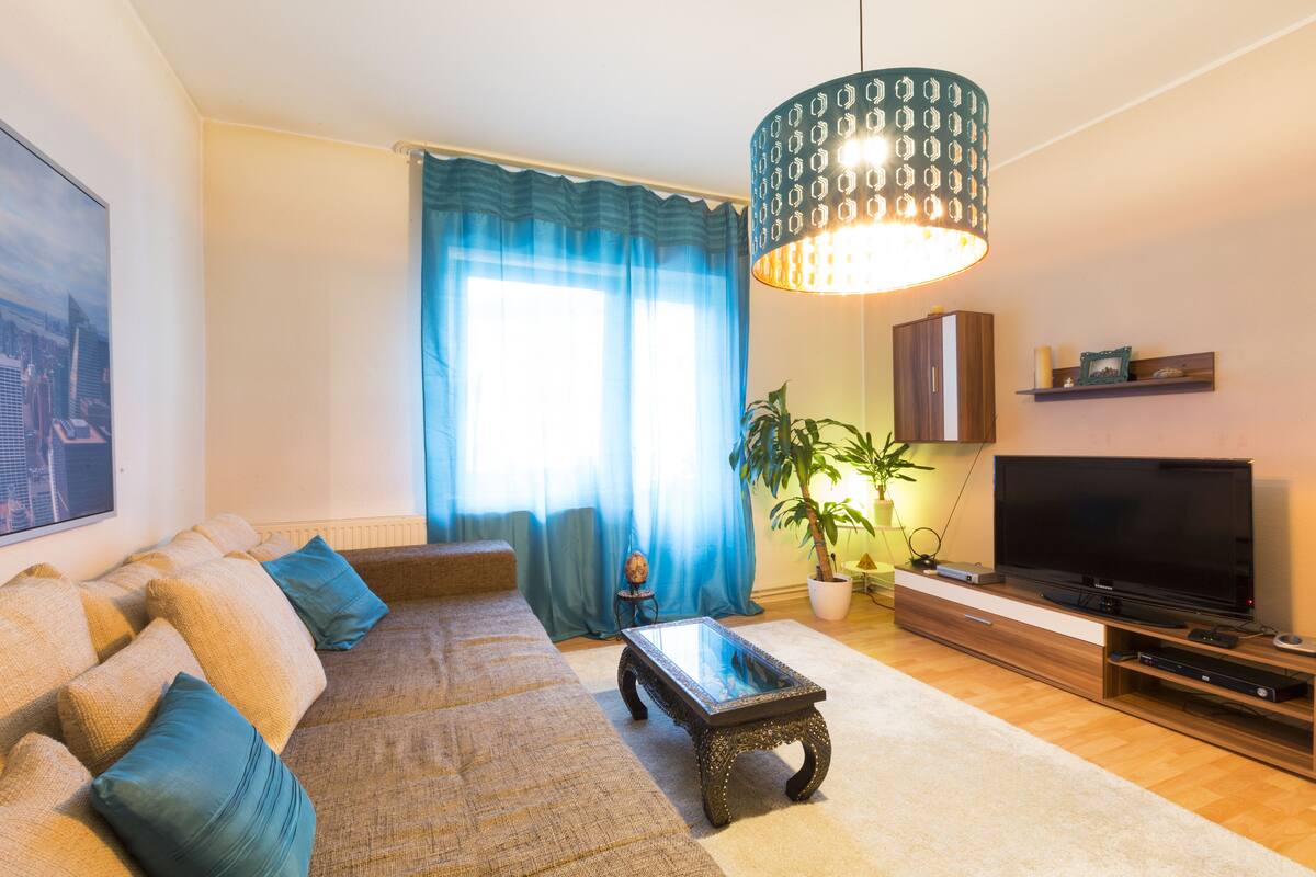A living room with a sofa, coffee table, TV, and a large window with curtains.