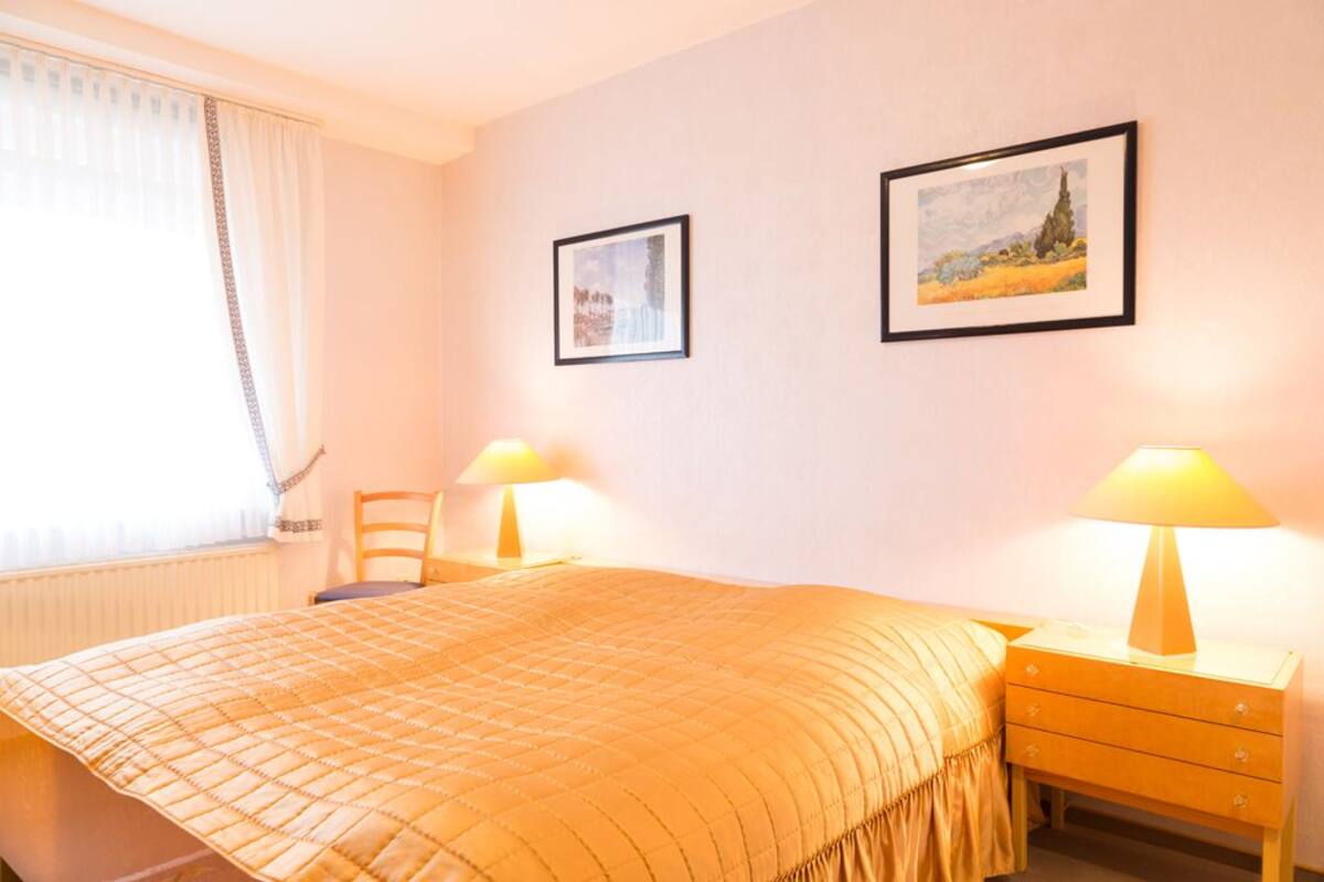 A hotel room with a bed, two bedside tables with lamps, a chair, and two framed pictures on the wall.