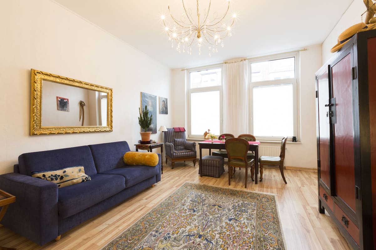A living room with a blue sofa, a patterned rug, a wooden cabinet, and a chandelier.