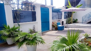 A courtyard with potted plants, a blue and white wall, and a blue chair under an umbrella. - Appartement Maképé B.M 2 (Douala)