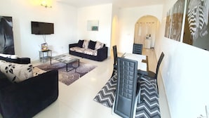 A modern living room with a sofa, coffee table, and dining area. - Appartement Maképé B.M 2 (Douala)